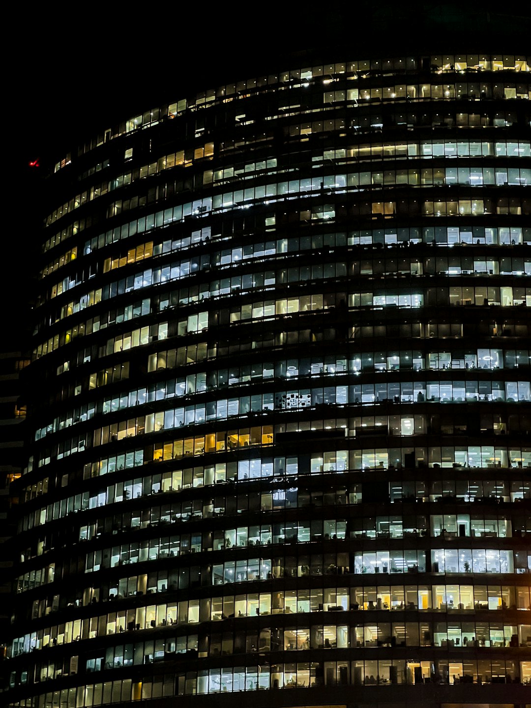Moderno edificio per uffici curvo illuminato da luci interne di notte.