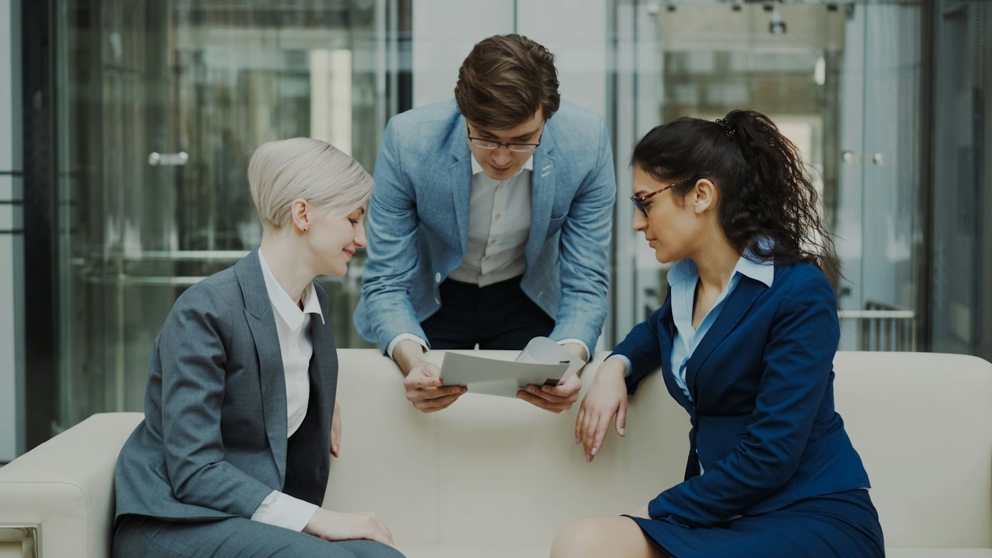 Un team di lavoro eterogeneo discute documenti su un divano in un ufficio moderno.